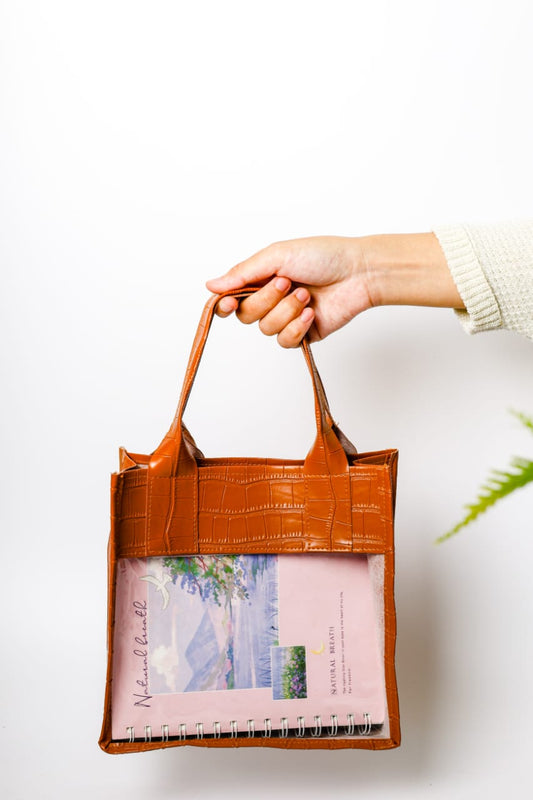 Hand holding a brown leather tote bag with a pink interior on a white background